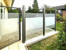 Zaunbau Transparente Glaszaun-Elemente mit Metallrahmen, umgeben von Pflanzen und einem Gehweg.