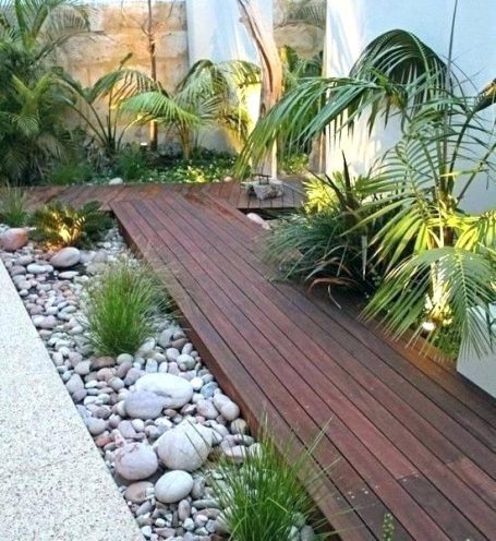 Gartenbau Gartengestaltung Landschaftsgestaltung Holzdeck umgeben von Pflanzen und Steinen in einem modernen Garten.